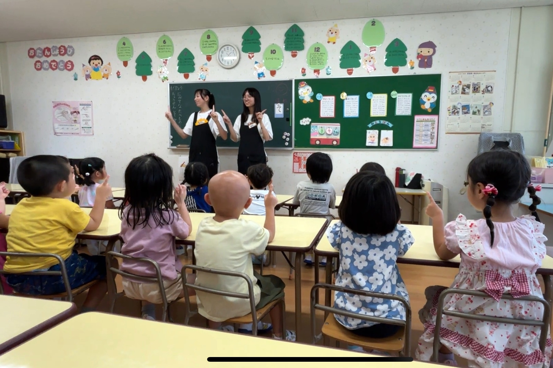 圖為亞大幼教系錢妤蓁（站立者右）、郭曉蓉（站立者左）同學，在日本實習時，以自編手指舞單元教導幼兒律動。